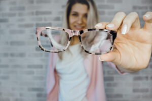 A blurred image of a woman holding a pair of eyeglasses up to the camera.