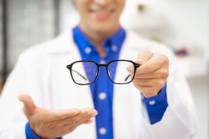Picture of an eye doctor holding a pair of glasses with black frames.